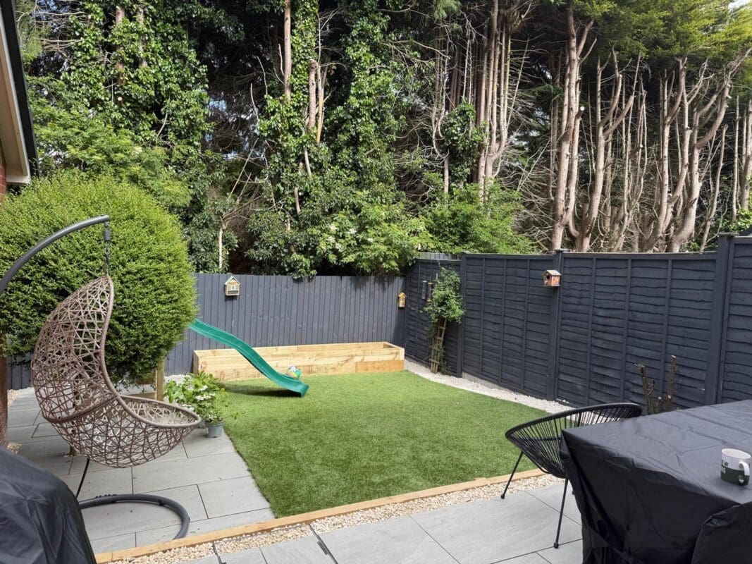 Residential garden landscaping project in Worcestershire — artificial lawn with timber edging, porcelain patio, hanging egg chair, and topiary ball shrub